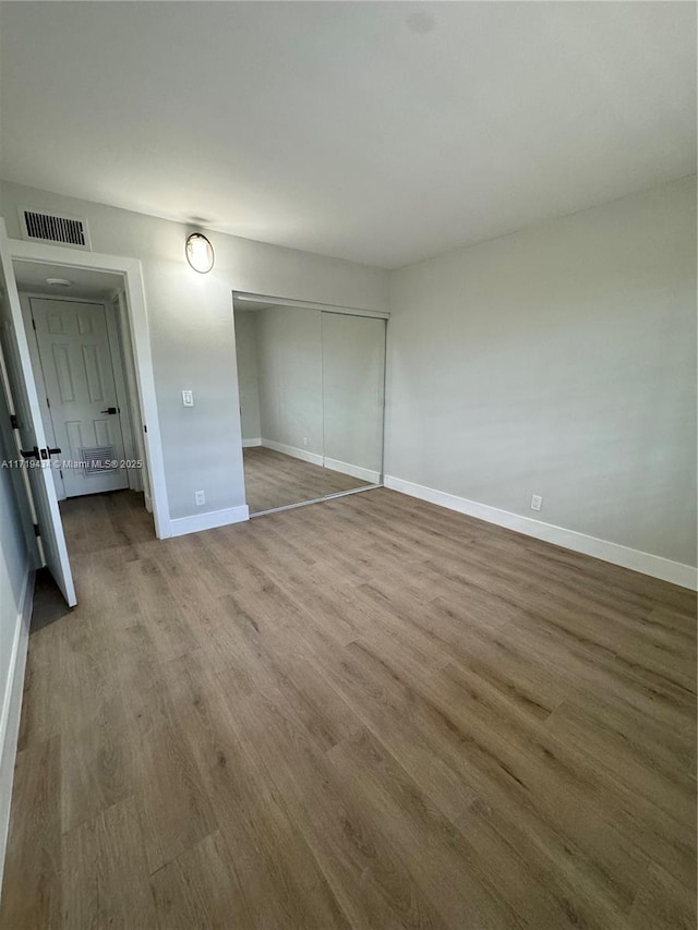 unfurnished bedroom featuring a closet, visible vents, baseboards, and wood finished floors