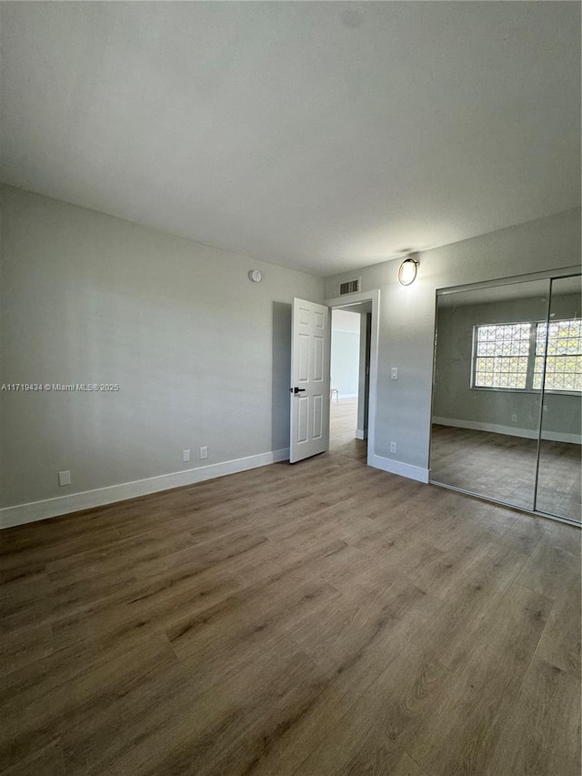 unfurnished bedroom with a closet, wood finished floors, visible vents, and baseboards