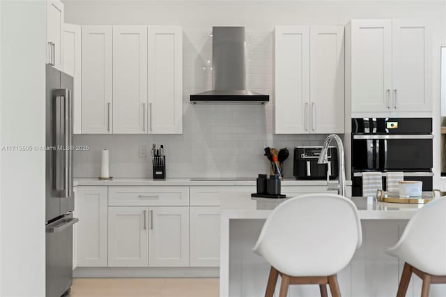 kitchen with a kitchen breakfast bar, stainless steel fridge, wall chimney range hood, and white cabinetry