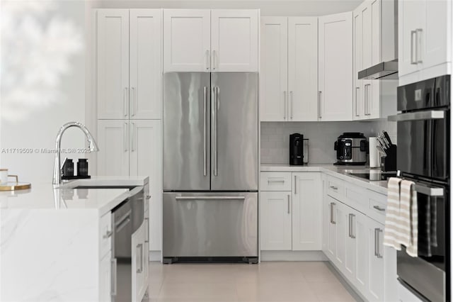 kitchen featuring light stone countertops, light tile patterned floors, backsplash, white cabinets, and appliances with stainless steel finishes