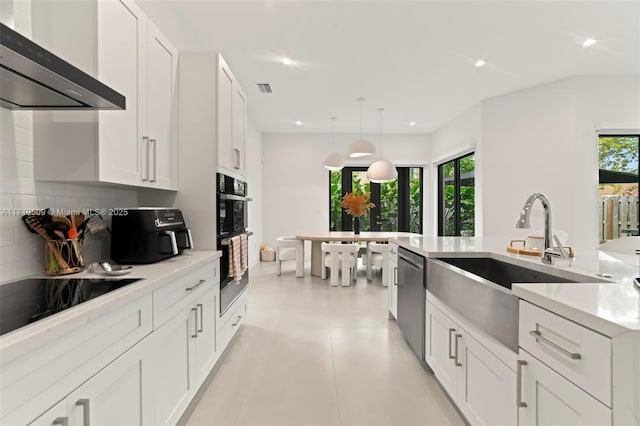 kitchen with sink, wall chimney exhaust hood, decorative light fixtures, white cabinets, and black appliances