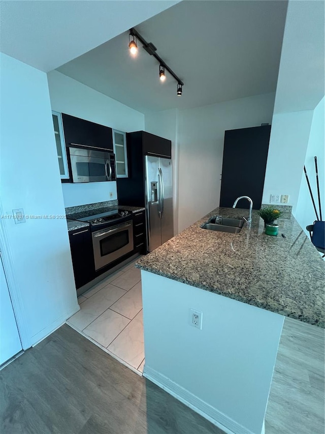 kitchen with kitchen peninsula, light wood-type flooring, stainless steel appliances, sink, and stone countertops