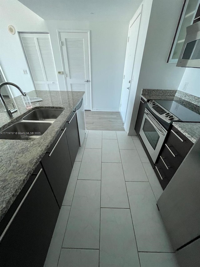 kitchen with sink, light tile patterned floors, dark stone counters, and appliances with stainless steel finishes