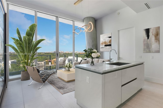 kitchen featuring expansive windows, sink, a center island with sink, an inviting chandelier, and white cabinetry