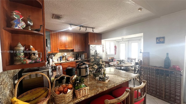 kitchen with tasteful backsplash, light stone countertops, track lighting, light tile patterned flooring, and a textured ceiling