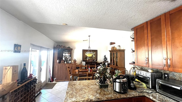 kitchen featuring vaulted ceiling, hanging light fixtures, light tile patterned floors, a textured ceiling, and stone counters