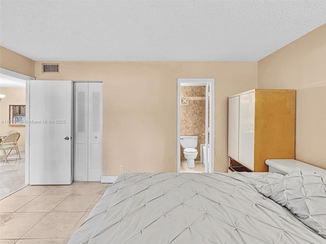 bedroom featuring a textured ceiling, a closet, ensuite bath, and light tile patterned floors