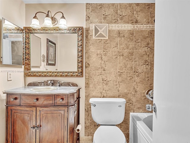 bathroom with tile walls, a tub to relax in, vanity, and toilet