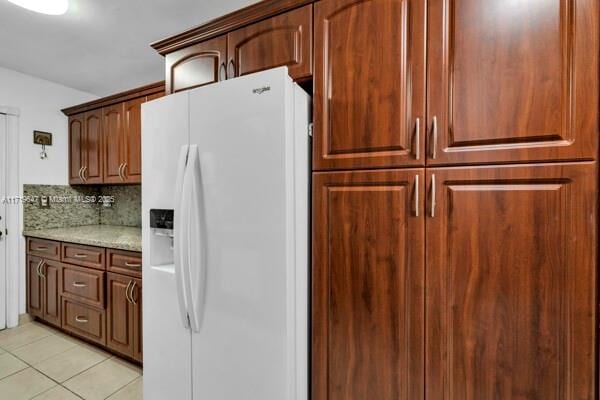 kitchen featuring backsplash, light stone counters, white fridge with ice dispenser, and light tile patterned floors