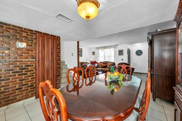 tiled dining space featuring a textured ceiling and brick wall