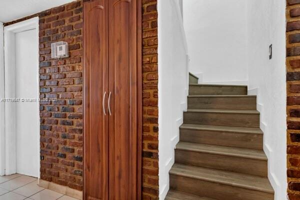 stairs featuring tile patterned flooring and brick wall