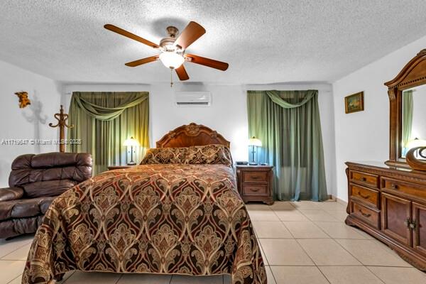 bedroom featuring ceiling fan, light tile patterned floors, a textured ceiling, and a wall unit AC