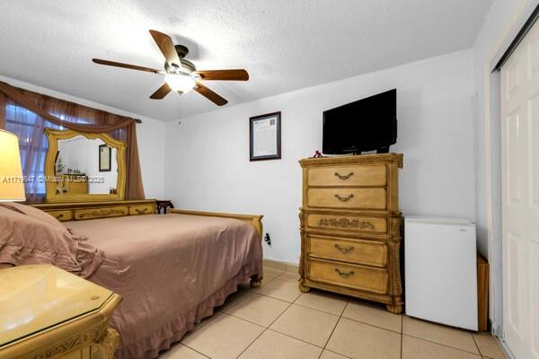 bedroom with ceiling fan, a closet, light tile patterned floors, and a textured ceiling