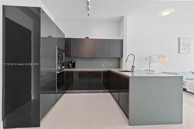 kitchen with kitchen peninsula, appliances with stainless steel finishes, rail lighting, sink, and light tile patterned floors