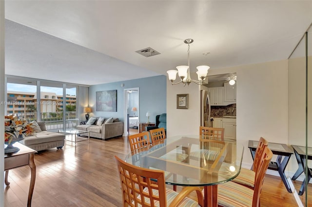 dining room featuring ceiling fan with notable chandelier, expansive windows, and light wood-type flooring