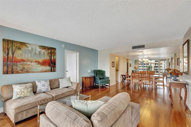 living room with an inviting chandelier, a textured ceiling, and light hardwood / wood-style floors