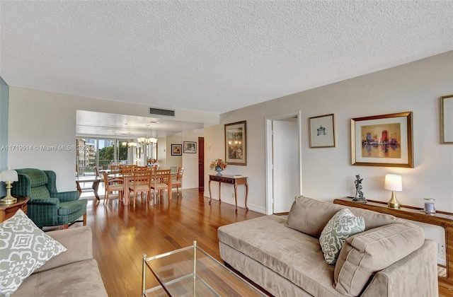 living room with a textured ceiling, a notable chandelier, and light hardwood / wood-style floors