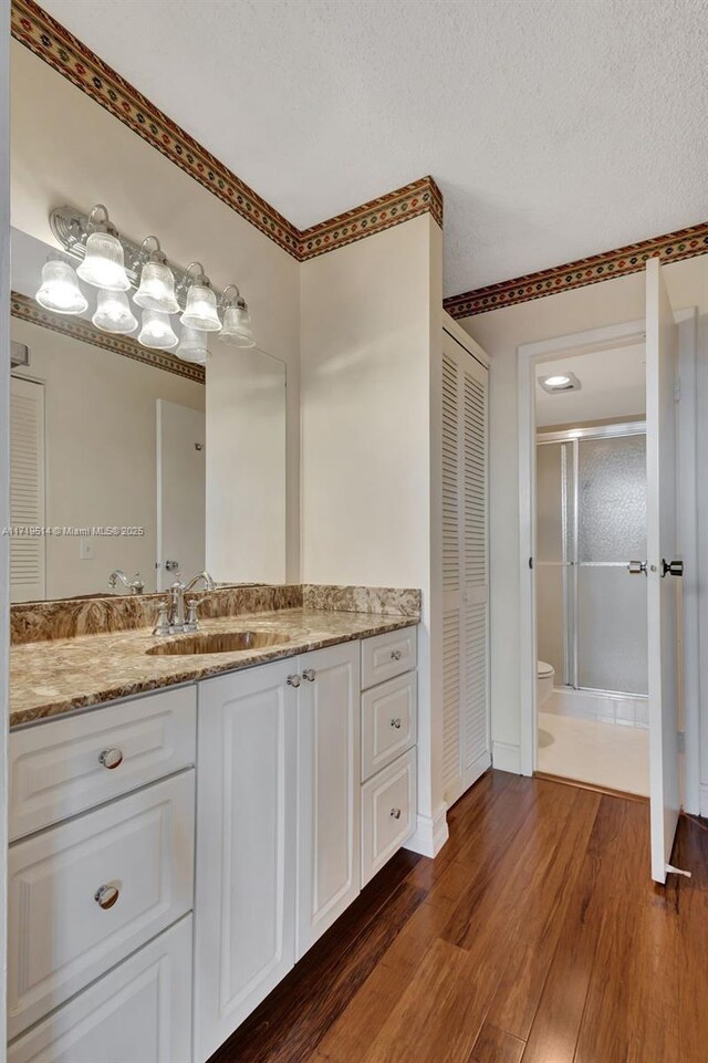 bathroom featuring hardwood / wood-style floors, vanity, a textured ceiling, a shower with shower door, and toilet