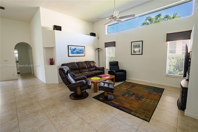 living room with ceiling fan, a towering ceiling, light tile patterned floors, and a textured ceiling