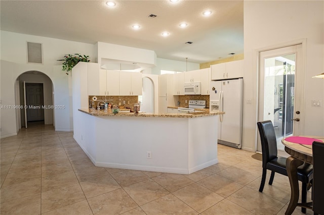 kitchen featuring kitchen peninsula, light stone countertops, backsplash, white appliances, and white cabinets