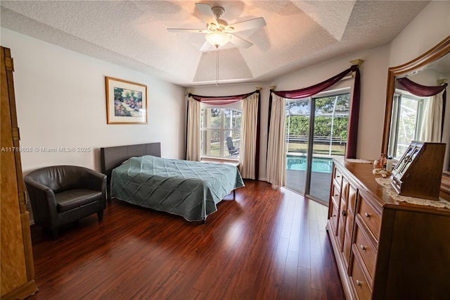 bedroom featuring access to exterior, dark hardwood / wood-style flooring, a textured ceiling, a raised ceiling, and ceiling fan