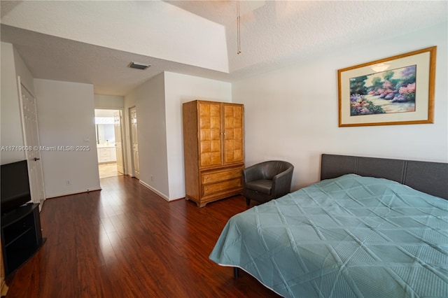 bedroom with a textured ceiling, dark hardwood / wood-style flooring, ensuite bath, and lofted ceiling