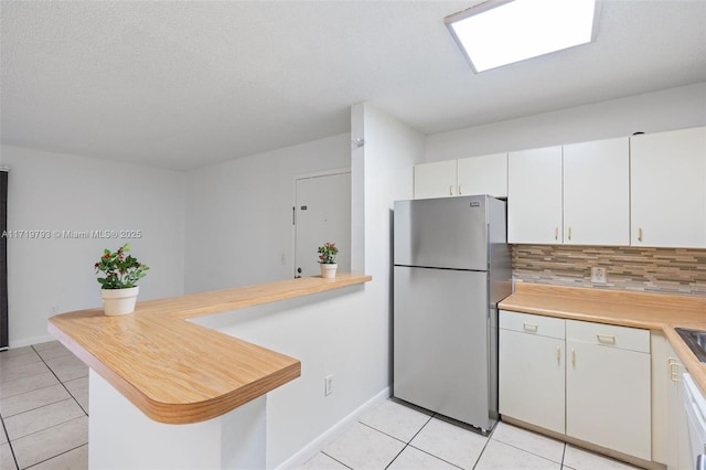 kitchen with kitchen peninsula, tasteful backsplash, white cabinets, stainless steel refrigerator, and light tile patterned flooring