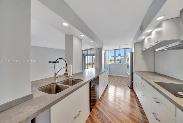 kitchen featuring sink, wall chimney exhaust hood, light hardwood / wood-style flooring, white cabinets, and black appliances