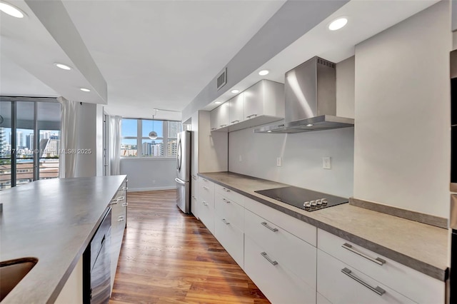 kitchen with stainless steel appliances, white cabinetry, wall chimney exhaust hood, and light hardwood / wood-style flooring