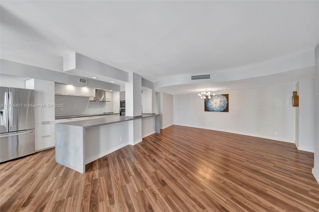 kitchen with white cabinetry, stainless steel fridge with ice dispenser, a notable chandelier, kitchen peninsula, and hardwood / wood-style floors