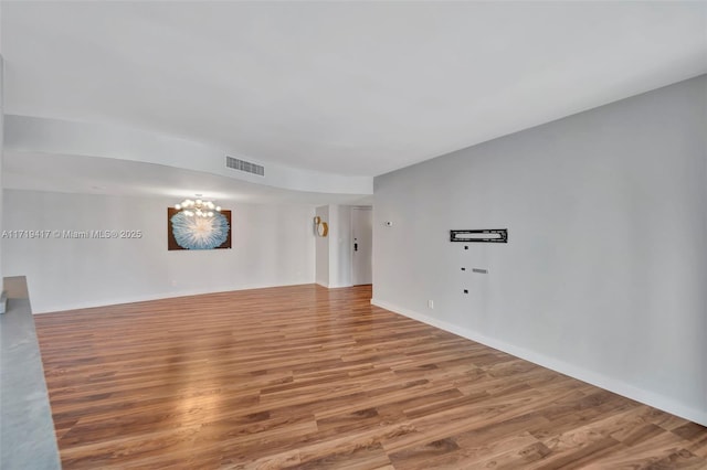 empty room featuring wood-type flooring and an inviting chandelier