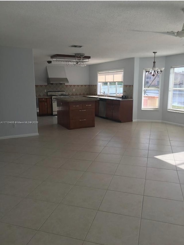 kitchen featuring pendant lighting, white range, wall chimney range hood, light tile patterned floors, and a chandelier