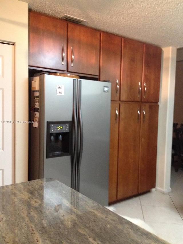 kitchen featuring a textured ceiling, light tile patterned floors, dark stone counters, and stainless steel refrigerator with ice dispenser