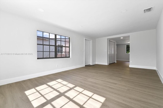 spare room featuring wood finished floors, a wealth of natural light, baseboards, and visible vents