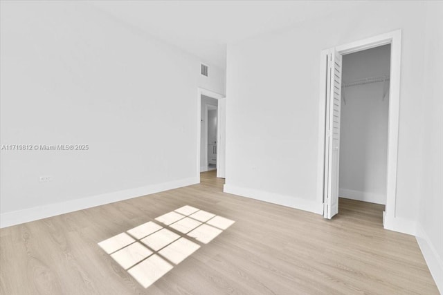 unfurnished bedroom featuring a closet, a spacious closet, baseboards, visible vents, and light wood-style floors