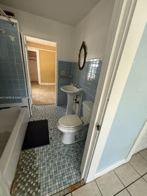 bathroom featuring a bath, tile patterned flooring, sink, toilet, and tile walls