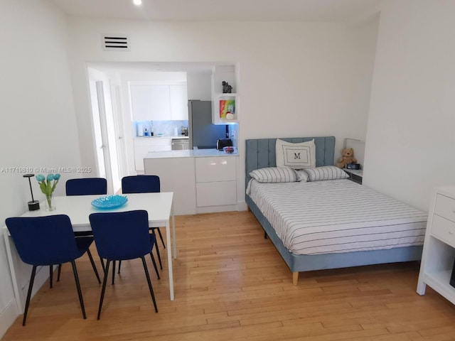 bedroom with stainless steel fridge and light hardwood / wood-style flooring