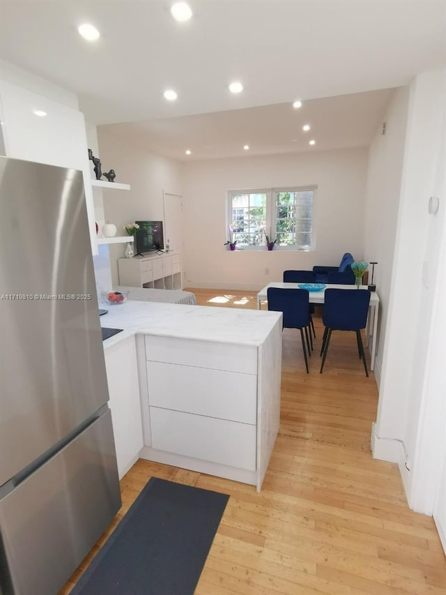 kitchen with stainless steel refrigerator, kitchen peninsula, white cabinets, and light hardwood / wood-style flooring