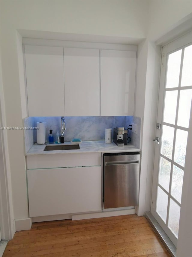 kitchen with decorative backsplash, light wood-type flooring, stainless steel dishwasher, sink, and white cabinetry