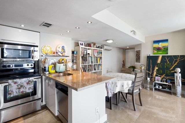 kitchen with white cabinets, sink, light stone countertops, kitchen peninsula, and stainless steel appliances