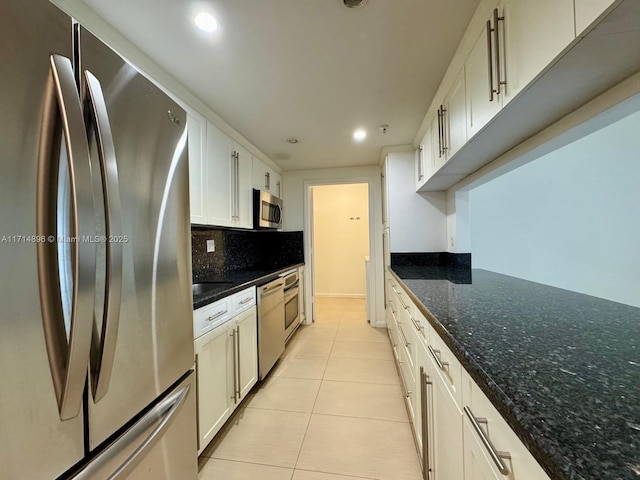 kitchen featuring dark stone countertops, light tile patterned floors, tasteful backsplash, white cabinetry, and stainless steel appliances