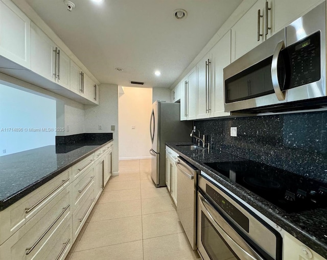 kitchen featuring backsplash, dark stone countertops, light tile patterned flooring, white cabinetry, and stainless steel appliances