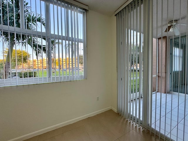 tiled empty room with a water view, a wealth of natural light, and ceiling fan