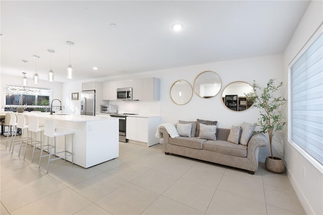 kitchen featuring a kitchen breakfast bar, stainless steel appliances, decorative light fixtures, a center island with sink, and white cabinets