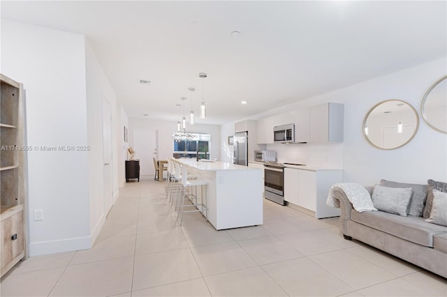 kitchen with a kitchen bar, stainless steel appliances, decorative light fixtures, white cabinetry, and a kitchen island