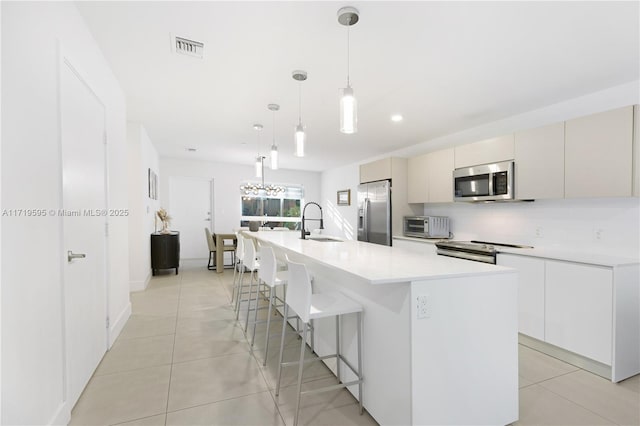 kitchen featuring decorative backsplash, stainless steel appliances, sink, decorative light fixtures, and a center island with sink