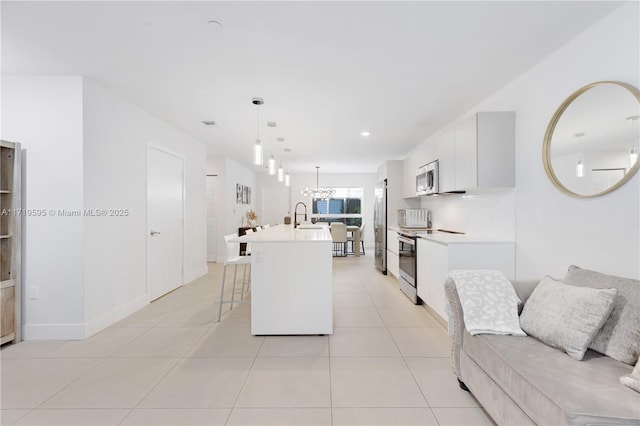 kitchen with pendant lighting, a kitchen island with sink, a breakfast bar area, white cabinetry, and stainless steel appliances