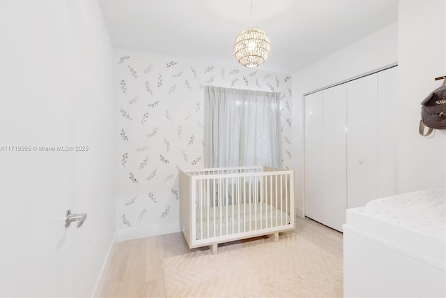 bedroom featuring wood-type flooring, a nursery area, a closet, and a notable chandelier