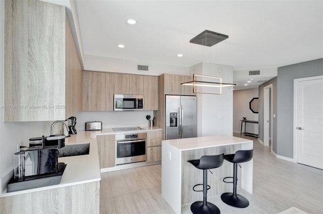 kitchen featuring a center island, light brown cabinets, hanging light fixtures, a breakfast bar, and appliances with stainless steel finishes