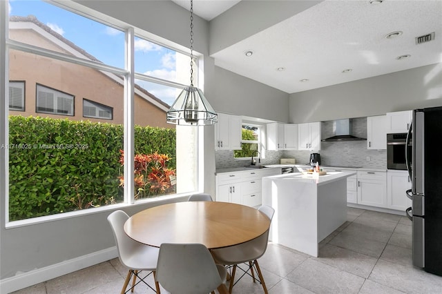 kitchen featuring wall chimney range hood, pendant lighting, white cabinetry, and appliances with stainless steel finishes